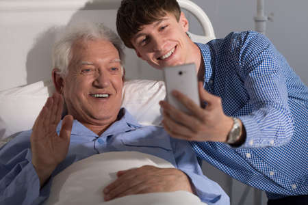 Teenage boy taking selfie with his grandpa in hospitalの写真素材