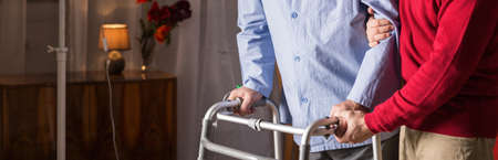 Older man walking with walker in caregiver's assistance