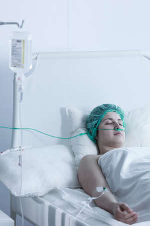 Vertical photo of young woman just after surgery in hospitalの写真素材
