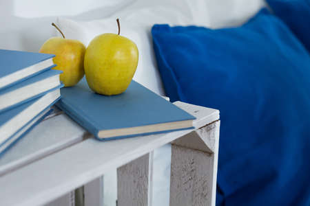 Green apple and books with blue covers lying on white, handmade nightstand