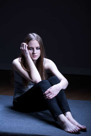 Sad girl sitting on floor in dark roomの写真素材