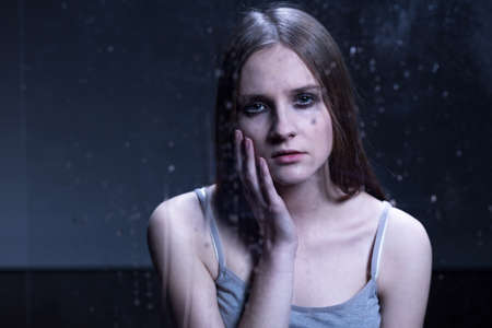 Sad girl with depression, feeling lonely, standing in dark roomの写真素材