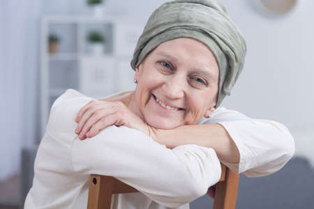 Cancer woman with headscarf sitting on chair, smiling