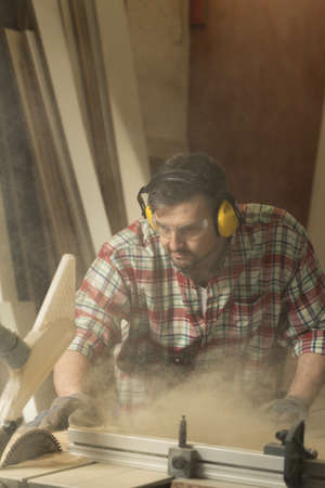 Craftsman in headphones and safety glasses during work in workshop