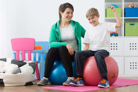 Boy and his instructor exercising on gym ballsの写真素材