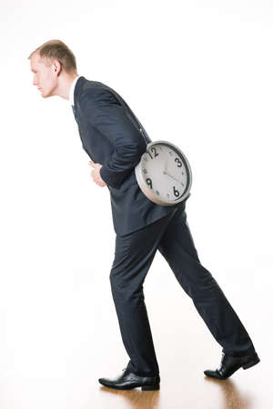 Man in suit carrying clock on his back, standing on white background.の写真素材