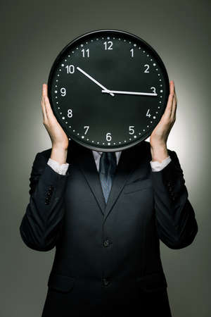 Man in black suit holding clock on head height, dark background.の写真素材