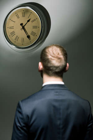 Man in suit back view and big clock hanging on wall.の写真素材