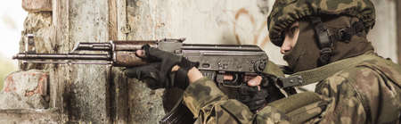 Young masked soldier is holding automatic weaponの写真素材