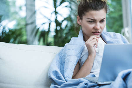 Sick woman with laptop on the sofaの写真素材