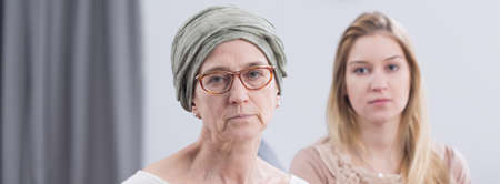 Sad and tired cancer woman with headscarf and blonde girl in background, panoramaの写真素材