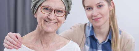 Smiling cancer woman embraced by young blonde girl, panorama.