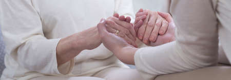 Two women in white clothes holding their hands, close up, panorama.
