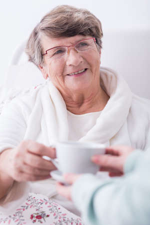 Senior sick woman in hospital drinking hot teaの写真素材