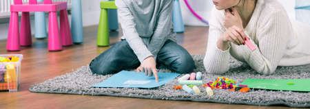 Boy and teacher during home lesson drawing a picture, lying on carpet, panorama.の写真素材