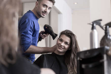 Beautiful smiling woman and her hairdresserwith a hairdryerの写真素材