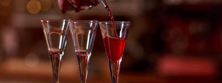 Barman pouring red sweet liqueur into glasses