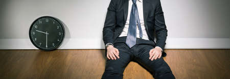 Man in suit sitting on floor next to clock, panorama.の写真素材