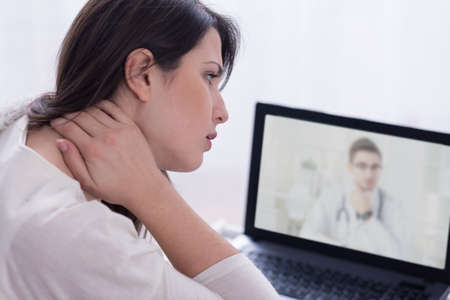 doctor and woman with neck pain in front of laptopの写真素材