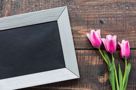 Shot of pink tulips and a frame laying on a plank table