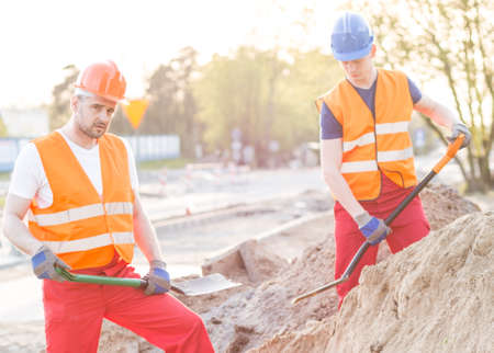 Photo of strong workers standing with shovels on building areaの写真素材