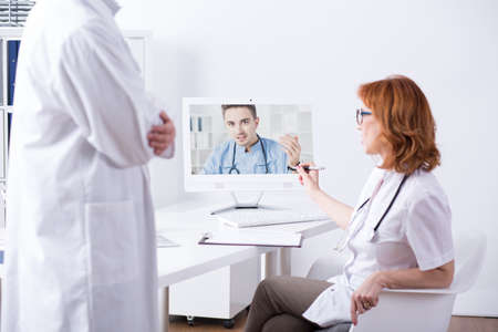 Man and woman in medical uniforms, talking via internet with young doctor
