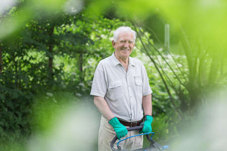 Elderly gardener is standing with lawnmower smilingの写真素材