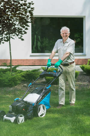Senior gardener is mowing lawn in front of his houseの写真素材