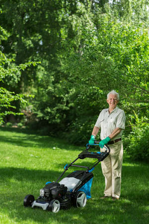 Elderly gardener is standing with the lawnmowerの写真素材