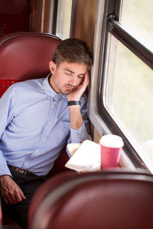 Tired young man sleeping in train during rideの写真素材