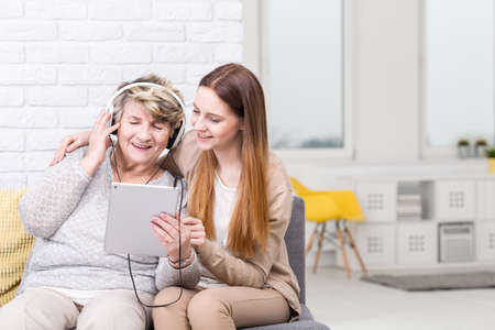 Shot of a senior woman listening to music and her granddaughter sitting next to herの写真素材