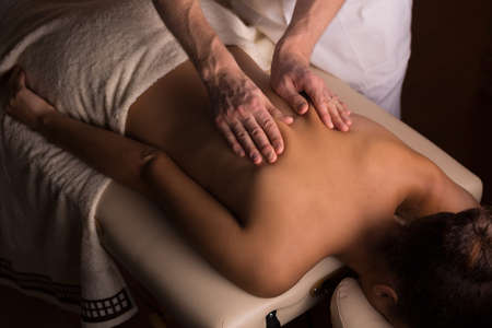 Masseur kneading the muscles on woman's back during therapeutic massageの写真素材