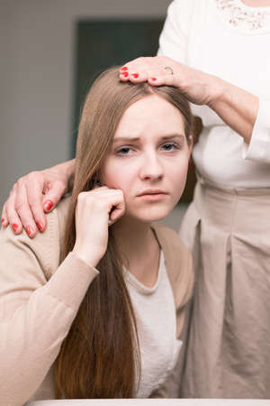 Worried teenage daughter in adolescence age hugged by her supportive motherの写真素材
