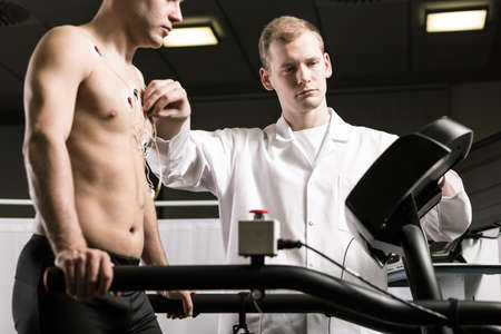 Sportsman standing on treadmill during medical examination and doctor in white uniform