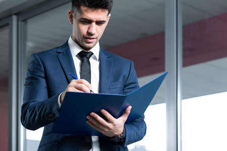 Businessman reading documents, standing in office buildingの写真素材