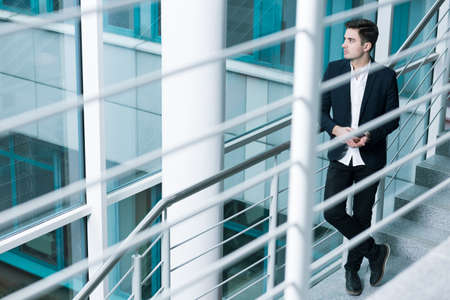 Graduate in suit, standing on stairs of a modern buildingの写真素材