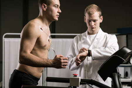 Man running on treadmill during medical test and medic in white uniform