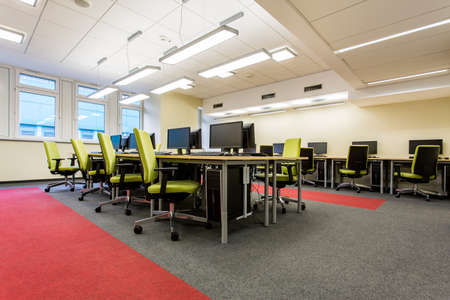 Modern classroom with wood desks, computers and comfortable green chairs