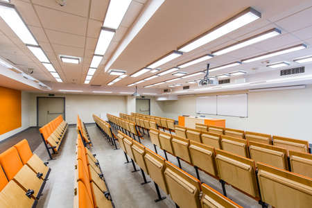 Spacious auditorium with orange, wood chairs and desk