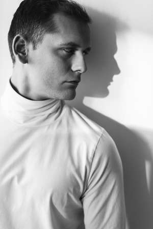 Young, sad man standing against the wall, photo in black and white