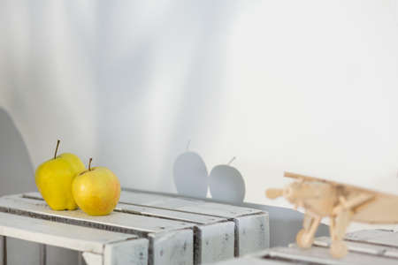 Two yellow apples on wooden box giving shadows on white wallの写真素材