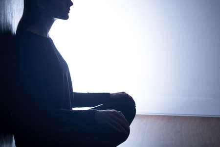 Teenage girl with depression closed alone in her dark room. Leaning on the wall