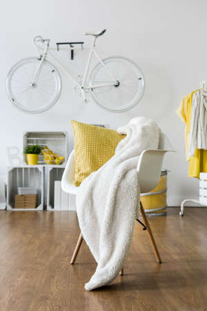 Yellow pillow and white blanket left on white armchair in loungeの写真素材