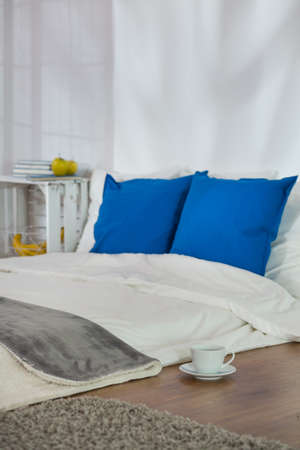 Mattress on wooden parquet with blue pillows. On floor cup of hot teaの写真素材