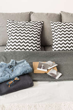 Clothes and pictures lying on bed with light bedding.