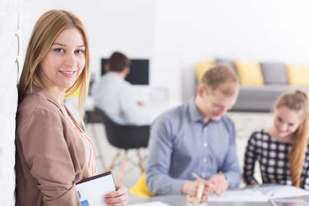 Young woman smiling, in the background people working together in light office