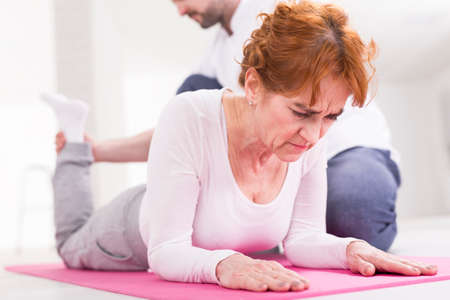 Woman with grimace effort lying on floor during exercises with physiotherapist