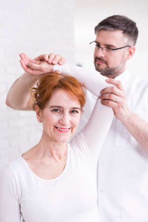 Mature, happy woman and physiotherapist exercising in light interior