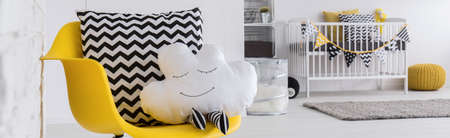 Baby room with yellow chair and decorative pillow, cot in the backgroundの写真素材