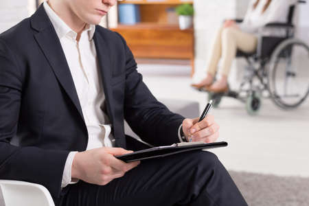 Cropped picture of a psychologist writing down notes and his patient sitting on a wheelchairの写真素材